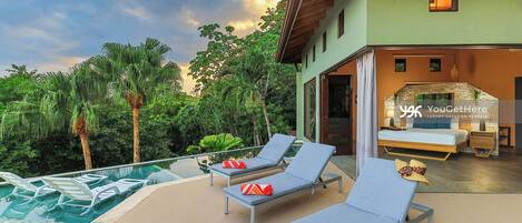 A modern villa with a pool, lounge chairs, and a bedroom with a large bed and a stone fireplace.