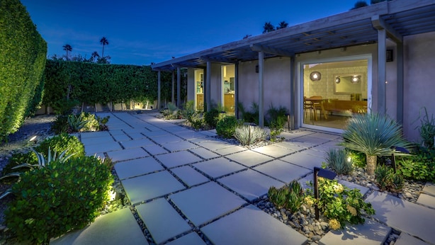 Una casa moderna con patio, illuminazione esterna e un giardino curato.