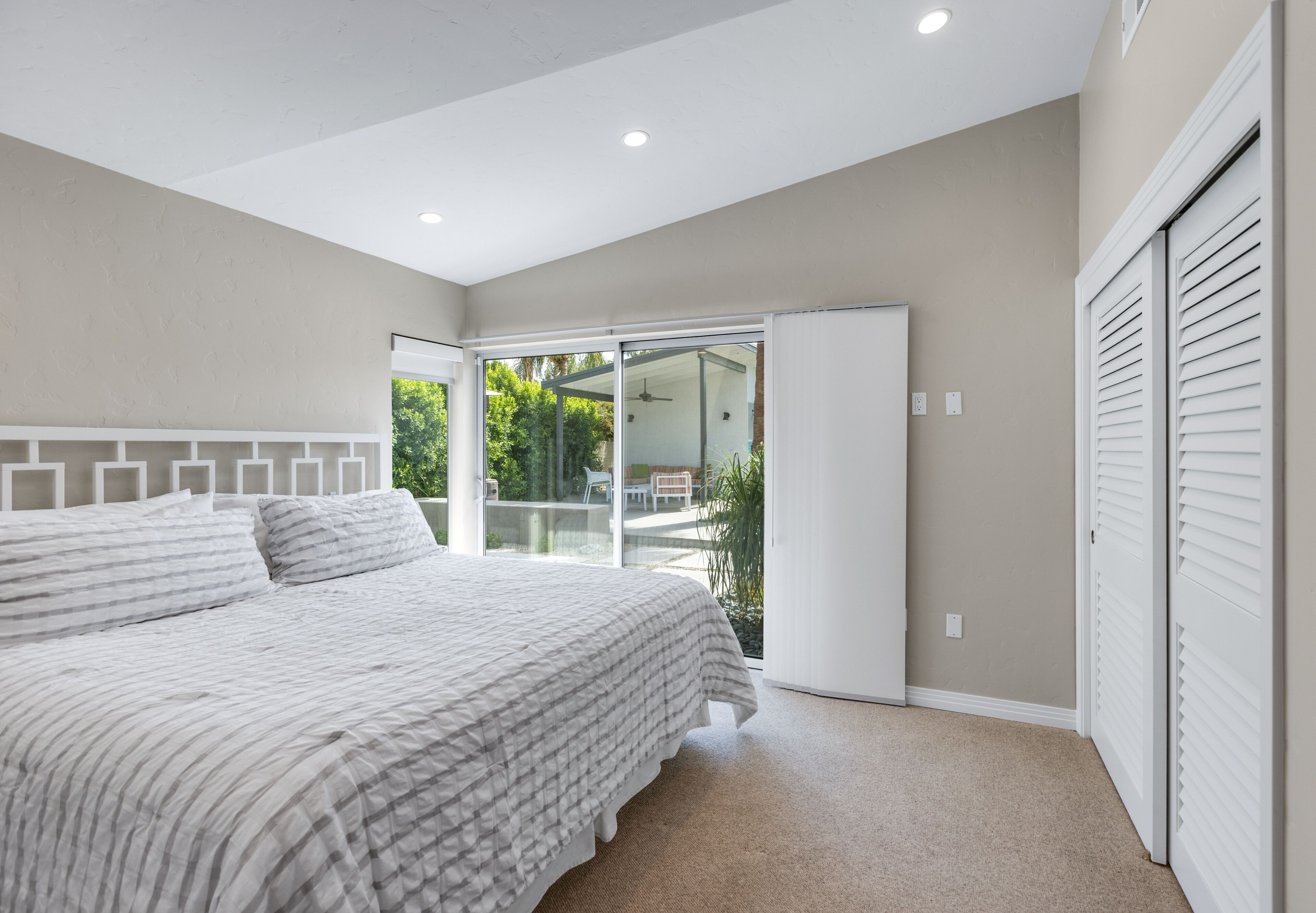 A bedroom with a large bed, a sliding glass door to a balcony, and a closet with louvered doors.