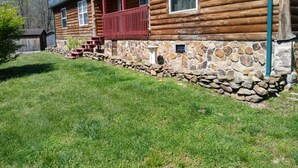A log cabin with a stone foundation, a red porch, and a stone wall. - The Sandstone log home 3BR 2BA (Genoa)
