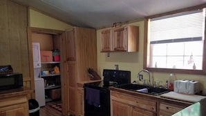 A compact kitchen with wooden cabinets, a stove, a sink, and a window with blinds. - The Sandstone log home 3BR 2BA (Genoa)