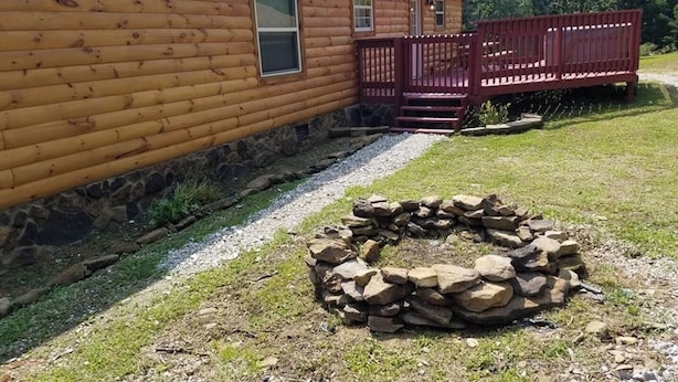 A log cabin with a stone foundation, a wooden deck, and a stone fire pit. - The Sandstone log home 3BR 2BA (Genoa)