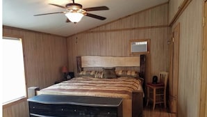 A bedroom with a bed, a dresser, a chair, a ceiling fan, and a window. - The Sandstone log home 3BR 2BA (Genoa)