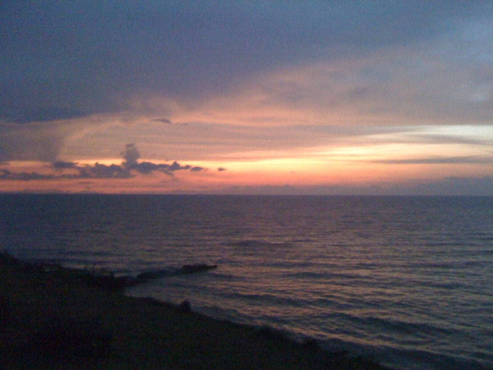 A coastal sunset with a calm sea and a distant shoreline.