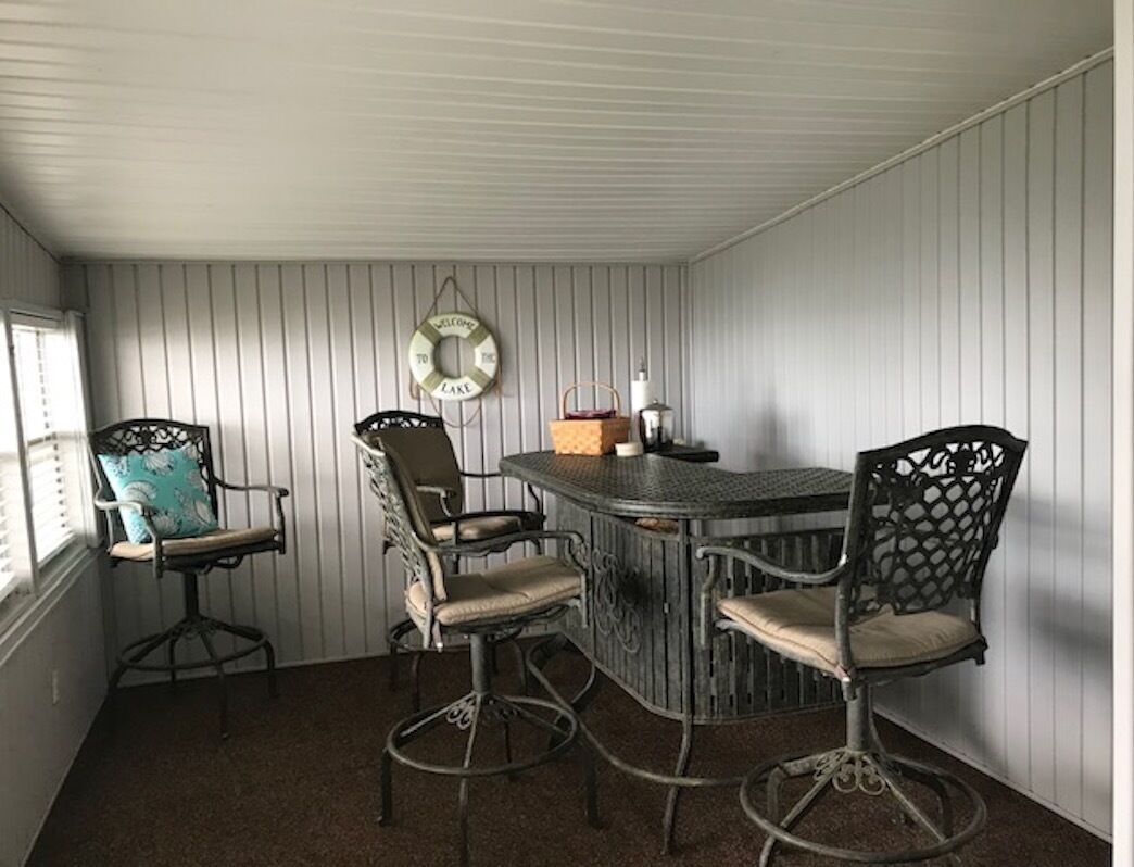 A dining area with a round table and four chairs, a wall-mounted sign, and a window with blinds.