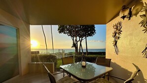 Un espace repas avec une table et des chaises en verre, une vue sur le coucher de soleil sur l’océan et des œuvres d’art décoratives sur les murs.