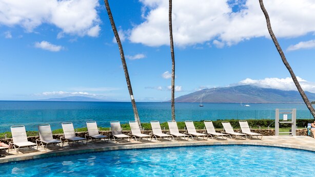 Une piscine dotée de chaises longues, offrant une vue sur l’océan et une montagne.