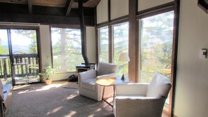 A cozy room with a fireplace, two armchairs, a small table, and large windows offering a view of the outdoors. - 2 Bedroom,+Loft, 2 Bath Condo, Amazing Views For Miles Accommodates 6. (Mammoth Lakes)