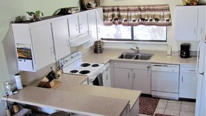 A compact kitchen with white cabinets, a stove, a sink, and a coffee maker. There are stools at the counter and a patterned rug on the floor. - 2 Bedroom,+Loft, 2 Bath Condo, Amazing Views For Miles Accommodates 6. (Mammoth Lakes)