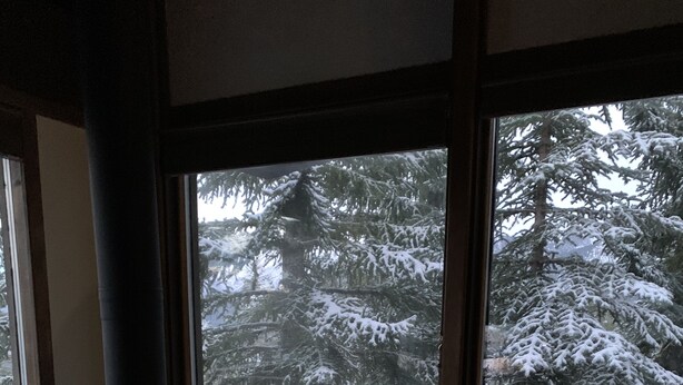 A cozy room with a wood-burning stove, large windows, and a view of snow-covered trees. - 2 Bedroom,+Loft, 2 Bath Condo, Amazing Views For Miles Accommodates 6. (Mammoth Lakes)
