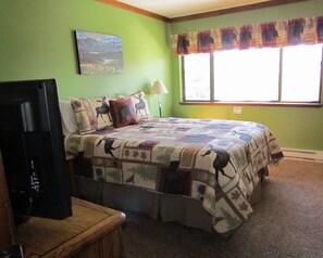 A bedroom with a bed, a television on a wooden stand, a lamp, and a window with a view of a landscape. - 2 Bedroom,+Loft, 2 Bath Condo, Amazing Views For Miles Accommodates 6. (Mammoth Lakes)
