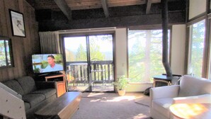 A living room with a television, a sofa, a chair, a small table, and a balcony with a view of trees and mountains. - 2 Bedroom,+Loft, 2 Bath Condo, Amazing Views For Miles Accommodates 6. (Mammoth Lakes)