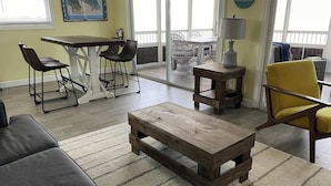 A living room with a wooden coffee table, a sofa, a yellow chair, a dining table with chairs, and a clock on the wall. - Tropical Paradise - Ocean front with swim spa (Cudjoe Key)
