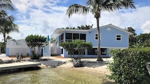 A two-story house with a clear view of the surrounding landscape, including a body of water and palm trees. - Tropical Paradise - Ocean front with swim spa (Cudjoe Key)