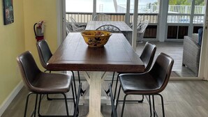 A dining area with a wooden table and chairs, a bowl on the table, and a view of the beach through large windows. - Tropical Paradise - Ocean front with swim spa (Cudjoe Key)