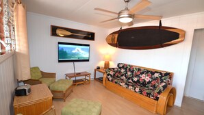 A living room with a wooden sofa, green armchairs, a television, and a ceiling fan. - Beautiful Lahaina Side 2 BR Condo with Beach View B7 (Honokowai)