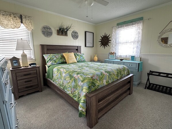 A bedroom with a wooden bed, a nightstand, a dresser, a vanity, and a window with curtains. - Ocean View Family Home! Games, Hammocks & Chill Space Underneath. Walk to Shops! (Ocean Isle Beach)