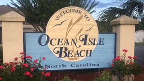 Velkomstskilt for Ocean Isle Beach, North Carolina, med et cirkulært design og en illustration af en strandscene.