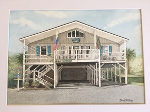 A two-story building with a balcony, a flag, and a sign indicating it's for rent. - Ocean View Family Home! Games, Hammocks & Chill Space Underneath. Walk to Shops! (Ocean Isle Beach)