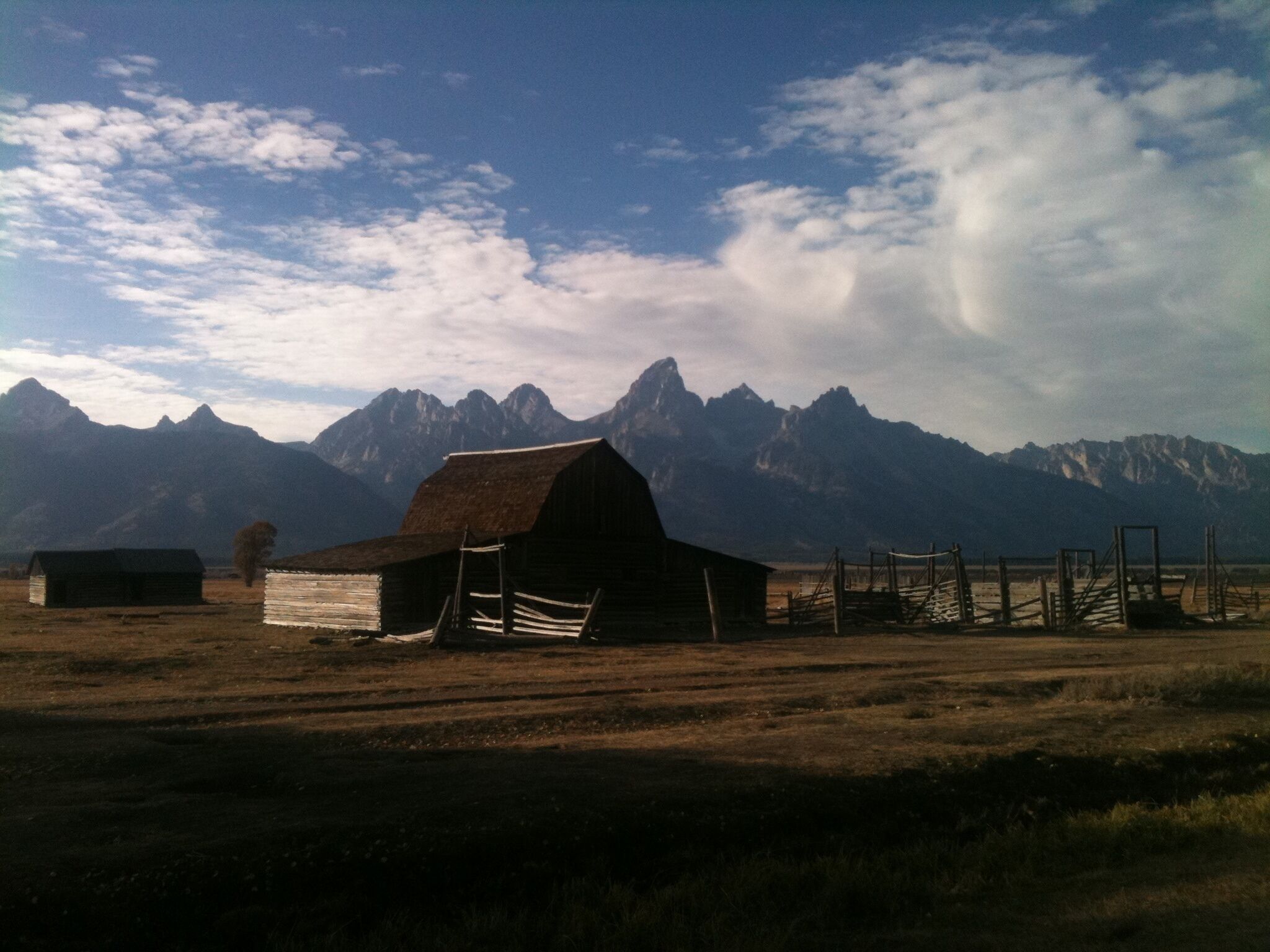 A rustic barn with a thatched roof in a rural setting, surrounded by mountains and open fields.