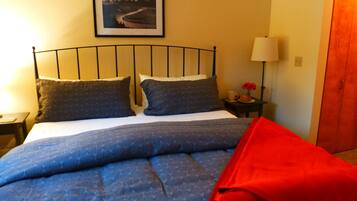 Una cama con estructura metálica, dos almohadas, una manta azul y un plaid rojo.