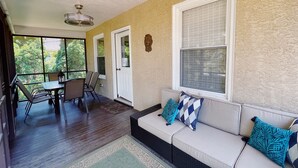 Un salón con ventanales, comedor, sofá con cojines estampados y vistas al exterior.