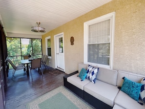 Relax in a cozy seating area with a sofa and dining table near a window offering a view of lush greenery.