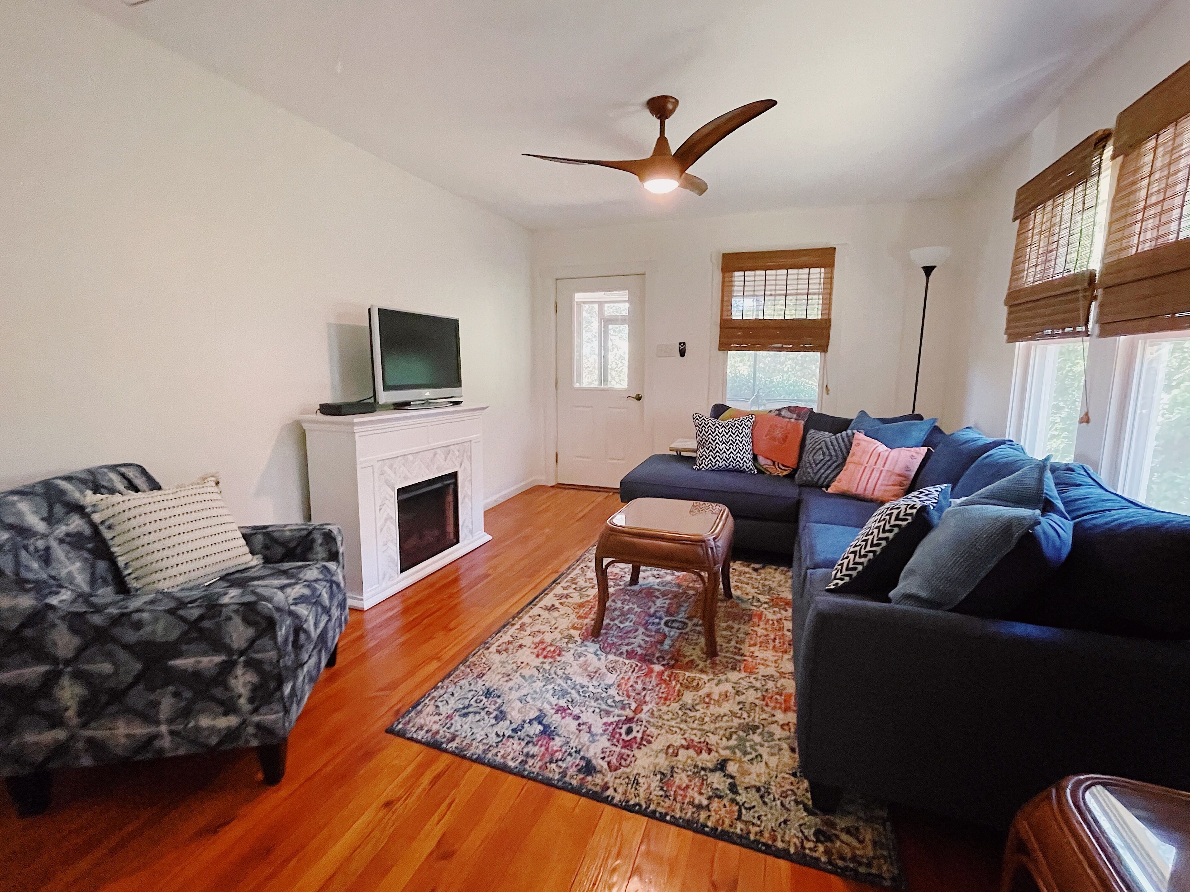 A living room with a fireplace, a sofa, a chair, a television, and a ceiling fan.