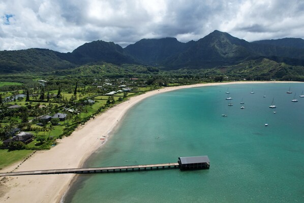 A coastal area with a beach, clear turquoise waters, and a pier extending into the sea. - Luxury Beachfront Home in Haena AC, Pool TVNC5141 (Hanalei)