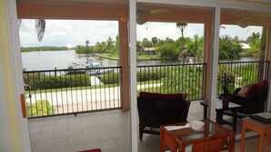 A balcony with a view of a lake, a boat, and greenery. - The Bokeelia Boathouse, waterfront, Boat Dock, Pine Island, Florida (Bokeelia)