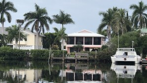 A waterfront property with a boat docked in the water, surrounded by palm trees and a house with a large balcony. - The Bokeelia Boathouse, waterfront, Boat Dock, Pine Island, Florida (Bokeelia)