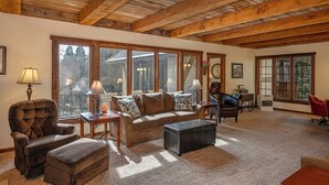 Ein gemütliches Wohnzimmer mit Holzboden, großen Fenstern, einer Couch, einem Sessel, einem Tisch und einem Kamin.