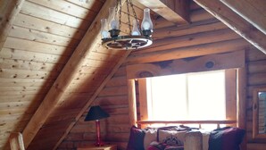 A cozy attic bedroom with a wooden bed, a nightstand, a lamp, and a window letting in natural light.
