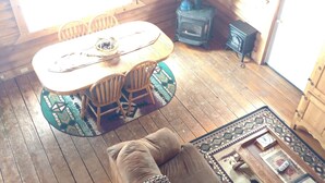 A cozy cabin interior with a wooden dining table, chairs, a sofa, a fireplace, and a large window.