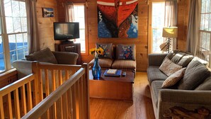 A cozy cabin interior with wooden walls, a television, a painting, and a sofa. - Clemson Football- Lake Hartwell Lakefront Cabin Private Dock 4 BR (Fair Play)