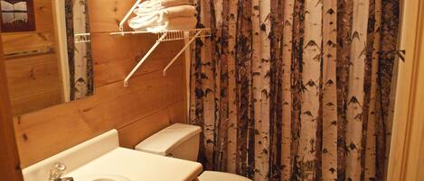 Baño de cabaña de madera con inodoro, lavamanos y repisa sobre el inodoro con toallas.
