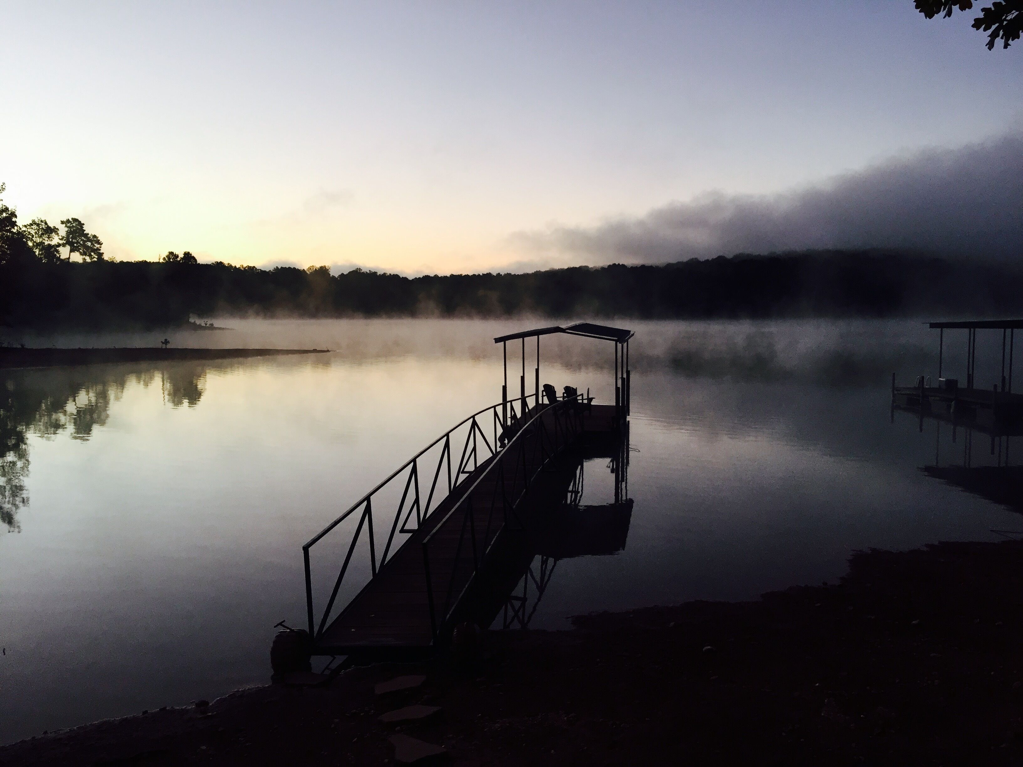 A pier extending into calm water with a covered seating area.