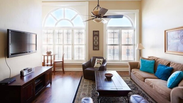 A living room with a TV, sofa, armchair, coffee table, and a ceiling fan.