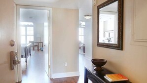 A hallway with wooden flooring, a black console table with a mirror, and a door with a key lock.