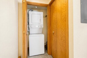 Una lavanderia con lavatrice e asciugatrice affiancate, una porta in legno e un tubo di ventilazione.