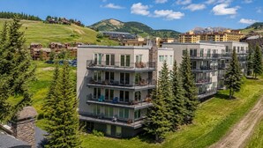 A multi-story hotel with balconies, surrounded by greenery and mountains.