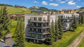 A multi-story hotel with balconies, surrounded by greenery and mountains.