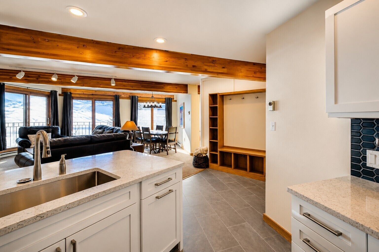 A modern kitchen with a central island, wooden ceiling beams, and a dining area with a view.