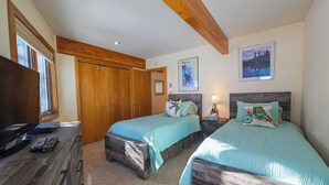 A bedroom with two beds, wooden headboards, a desk with a TV, and a window.