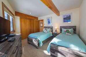 A bedroom with two beds, wooden headboards, a desk with a TV, and a window.