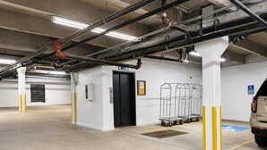 A parking garage with a white pillar, a black elevator door, and a car parked in the distance.