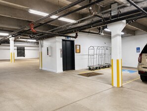 A parking garage with a white pillar, a black elevator door, and a car parked in the distance.