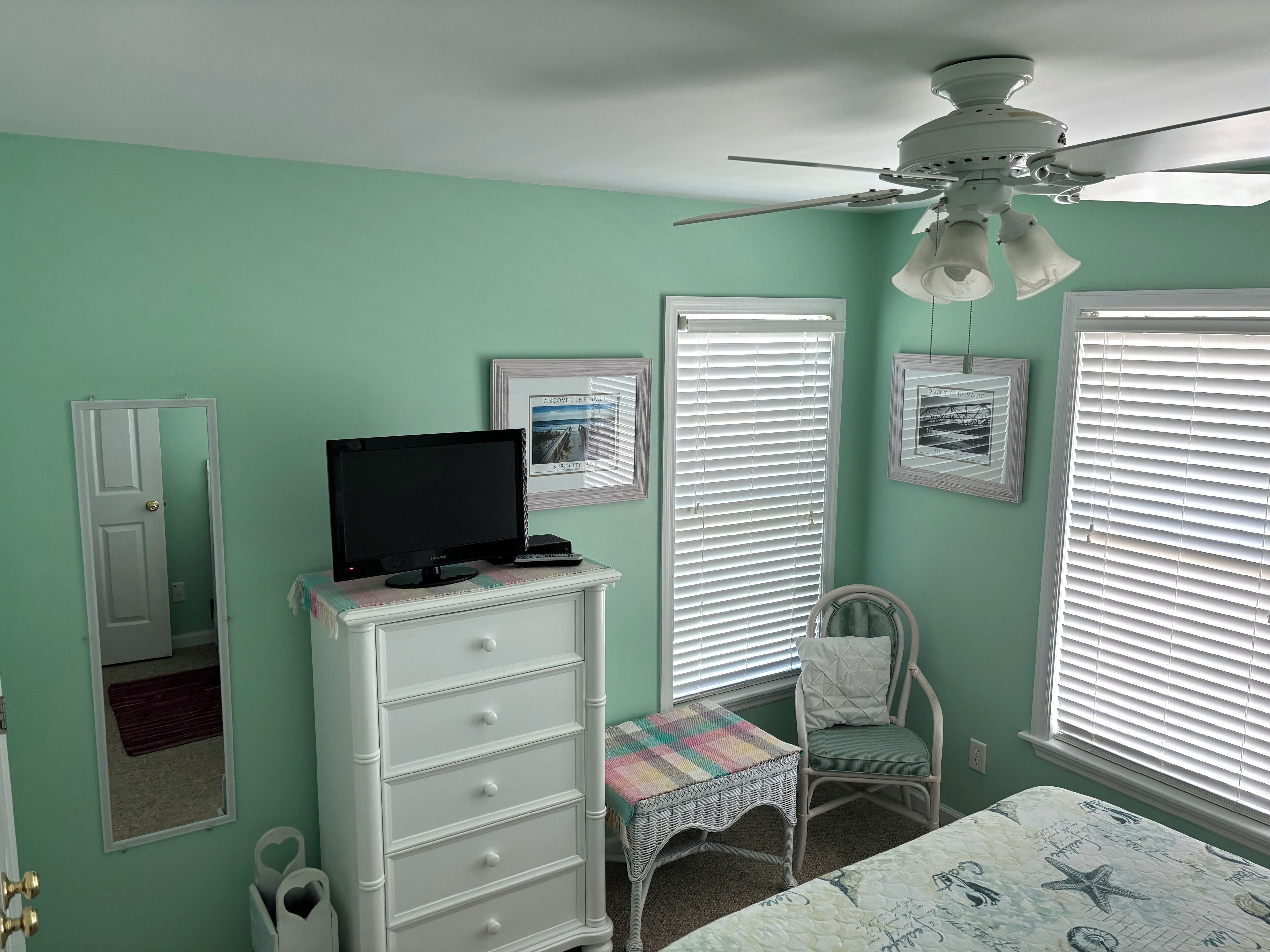 A bedroom with a bed, a dresser, a chair, a television, and a ceiling fan.