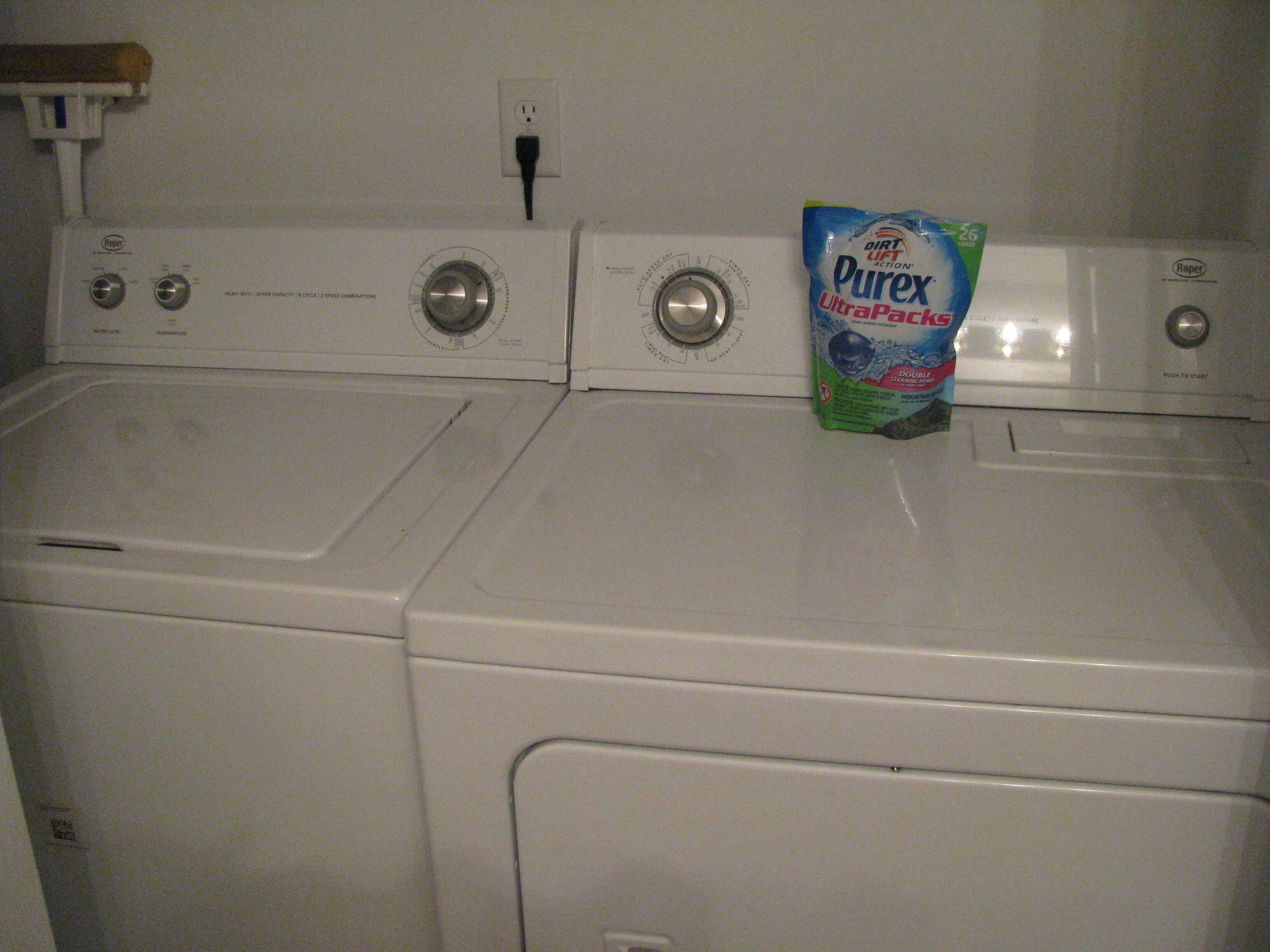 A front view of a double washer-dryer unit with control knobs and a power outlet above.