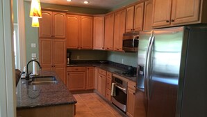 Una cocina con armarios de madera, un refrigerador de acero inoxidable, un microondas, un fregadero y una cafetera.